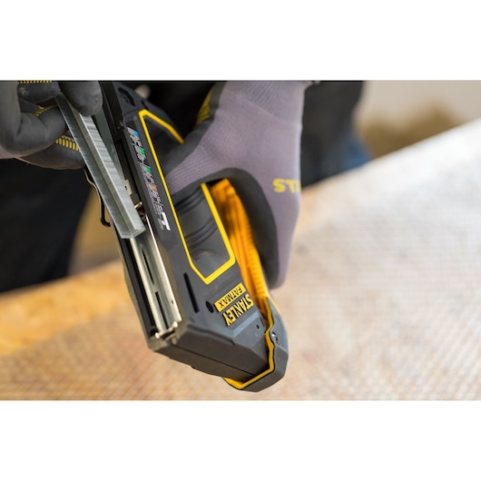 Photo of STANLEY FMHT0-80550 stapler held by gloved hand, loading staples, close-up view.