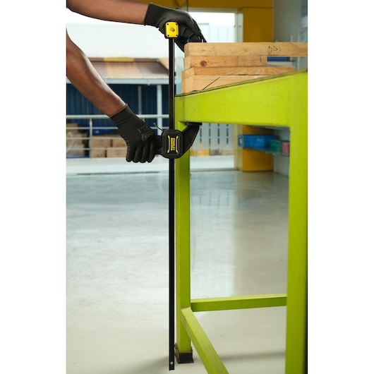 STANLEY FMHT0-83237 photography of bar clamp securing wooden boards to a bright green workbench.