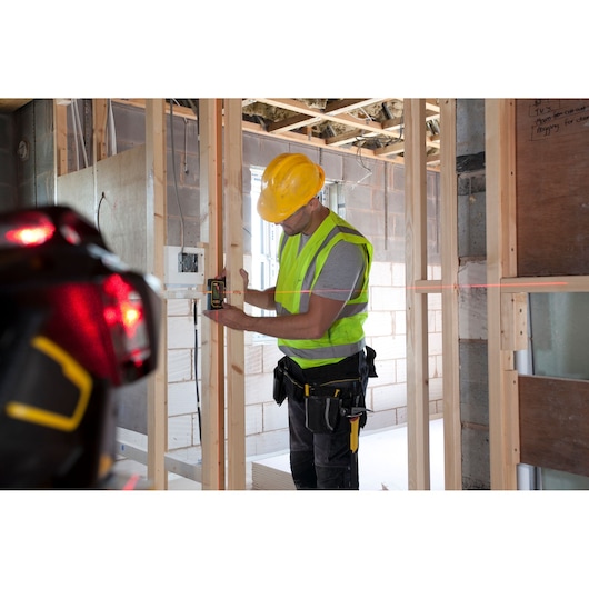 STANLEY FMHT1-77357 laser level used by worker in construction site, photography showing wall framing.