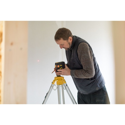 Stanley FMHT1-77413 laser level on tripod, person adjusting device in indoor setting.