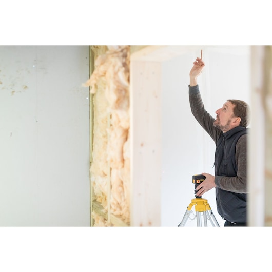 STANLEY FMHT1-77413 laser level on tripod used in interior construction, person marking wall.