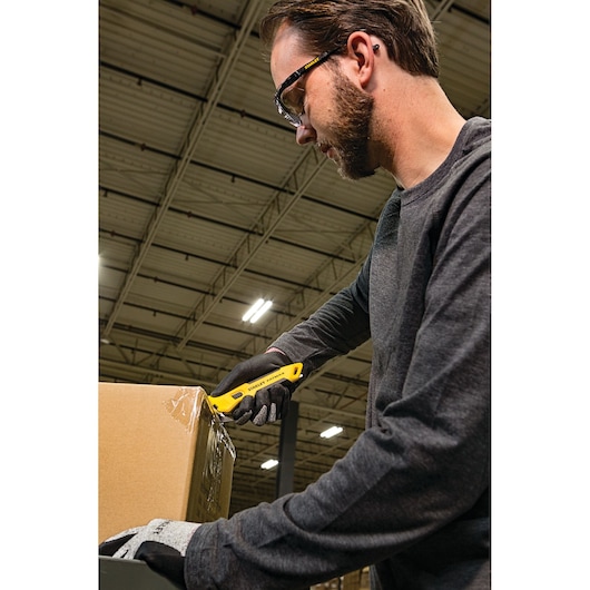 STANLEY FMHT10358 safety utility knife in use opening a cardboard box in a warehouse.
