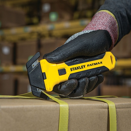 Stanley FMHT10361 FATMAX utility knife cutting box strap, close-up photo of tool held by gloved hand.