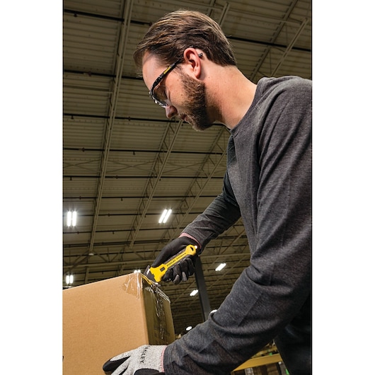 STANLEY FMHT10361 utility knife cutting cardboard box in warehouse, side angle photography.