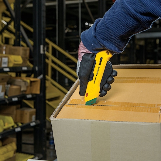 Stanley FMHT10363 utility knife used to cut tape on a cardboard box in a warehouse setting.
