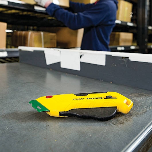 STANLEY FMHT10363 utility knife with yellow and black handle on warehouse table, side view.