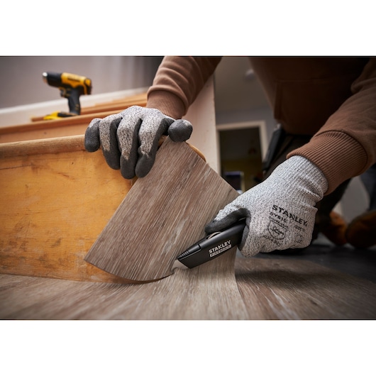 Photo of STANLEY FMHT10500-0 utility knife cutting vinyl flooring, close-up of gloved hands during installation.