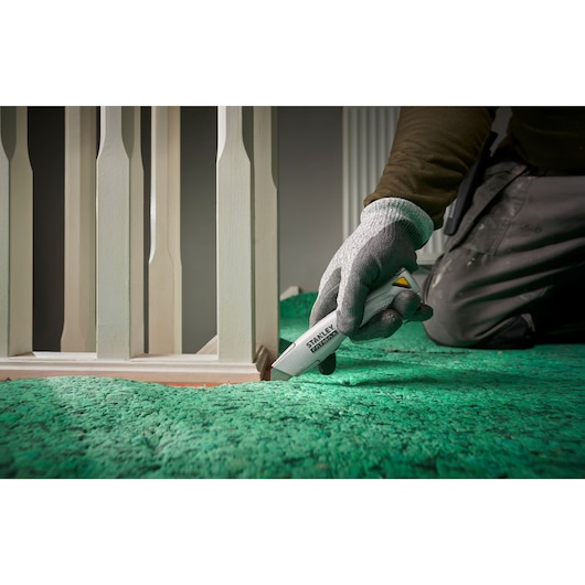Stanley FMHT10501-0 utility knife cutting green carpet near white banister, close-up photo.