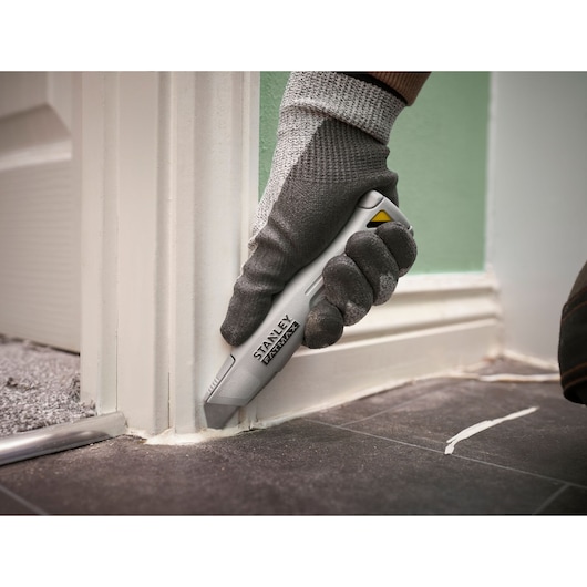 STANLEY FMHT10501-0 utility knife in use cutting sealant along baseboard on tiled floor.