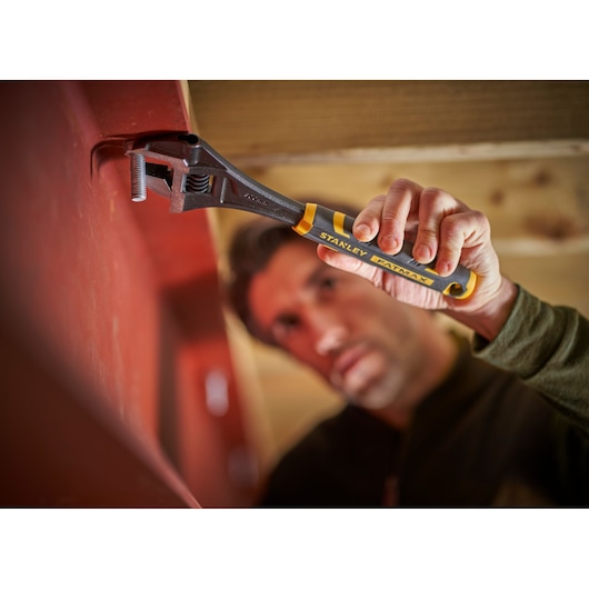 STANLEY FMHT13126-0 adjustable wrench with yellow-black handle in use tightening bolt on red surface.