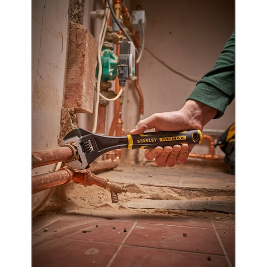 STANLEY FMHT13128-0 adjustable wrench with FATMAX handle used on copper pipes, close-up photo.