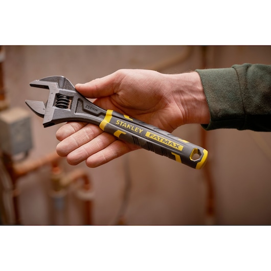 Stanley FMHT13128-0 adjustable wrench with yellow and black handle held in hand, indoor setting.