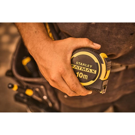 Photo of STANLEY FATMAX 10m tape measure FMHT33005-0 in hand, tool belt and tools in background.
