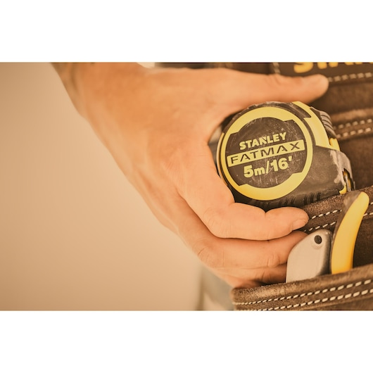 STANLEY FMHT33006-5 tape measure held by hand, yellow and black, close-up in tool belt.