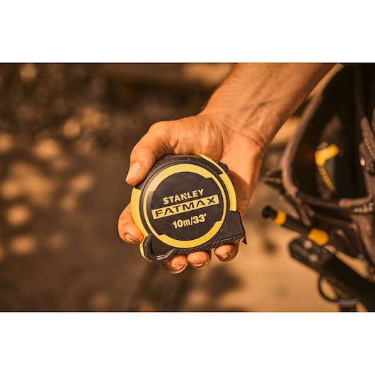 Photo of STANLEY FATMAX 10m/33' tape measure FMHT33104-5 in a worker's hand outdoors.