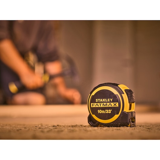 Photo of STANLEY FMHT33104-5 FATMAX tape measure, yellow and black, on a job site floor.