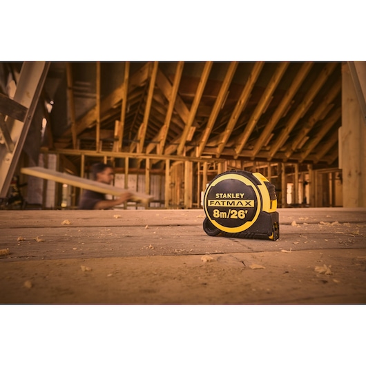 Photo of STANLEY FMHT33105-5 FATMAX 8m/26' tape measure on a wooden floor at a construction site.