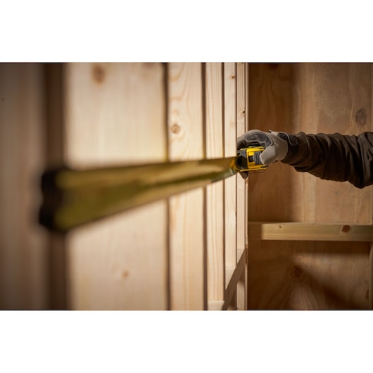 STANLEY FMHT33105 tape measure used to measure wood, close-up side angle, person wearing glove.
