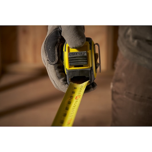 STANLEY FMHT33105 tape measure in use, yellow and black design, held by gloved hand, close-up view.