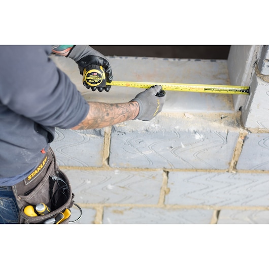 Photo of STANLEY FMHT36317-0 tape measure in use, measuring a concrete block window opening on a construction site.