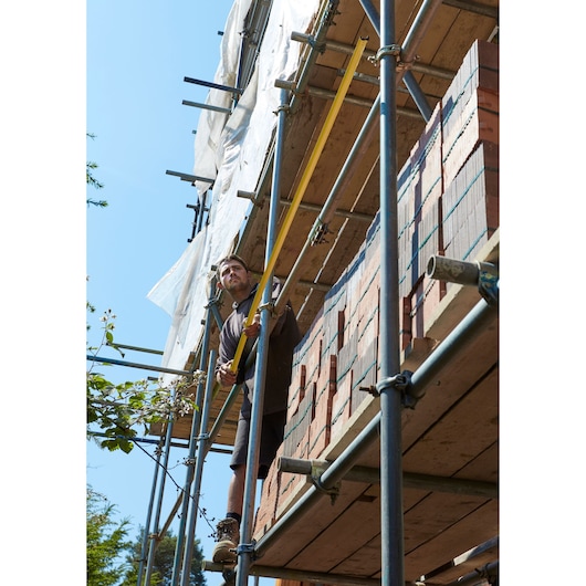 STANLEY FMHT36318-0 long yellow level used by worker on construction scaffolding near stacked bricks.