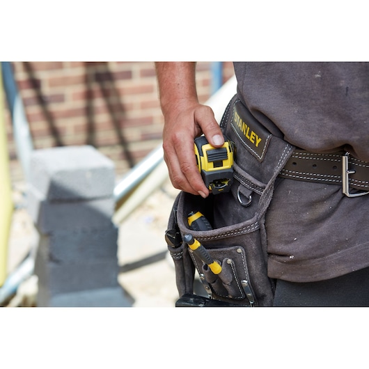 Photo of STANLEY FMHT36318-0 tape measure held by person wearing tool belt at construction site.