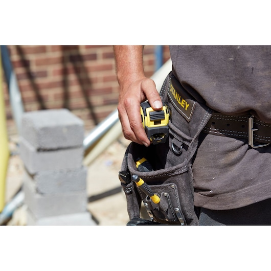 STANLEY FMHT36318-0 tape measure held by worker on tool belt, close-up, construction site background.