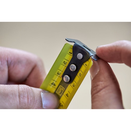 Close-up photo of STANLEY FMHT36318-0 tape measure end clasp and yellow measuring tape being held.
