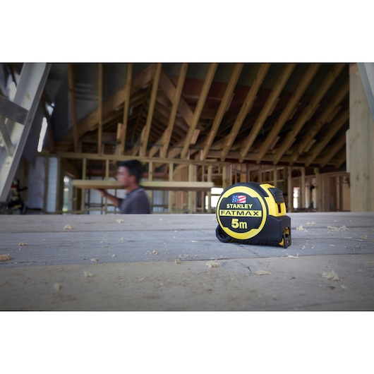 Photo of STANLEY FMHT36318-0 5m tape measure at a construction site with wooden framing in background.