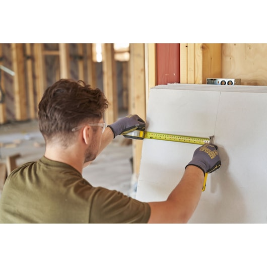 Photo of a person using a STANLEY FMHT38215-5 tape measure to measure drywall on a construction site.