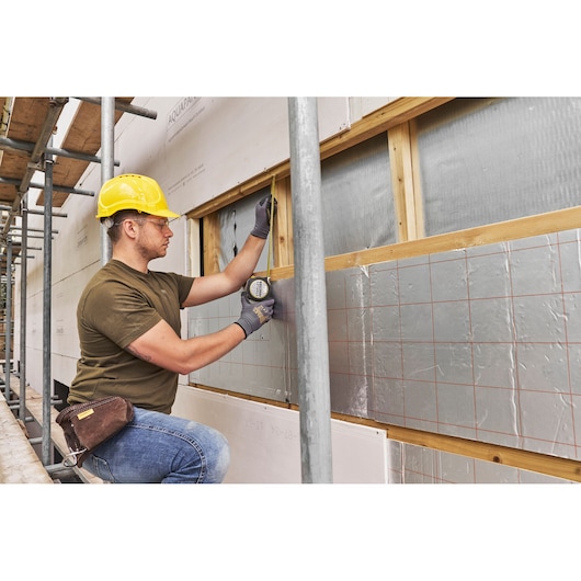 STANLEY FMHT38233-5 tape measure used by worker on construction site exterior wall, side angle.