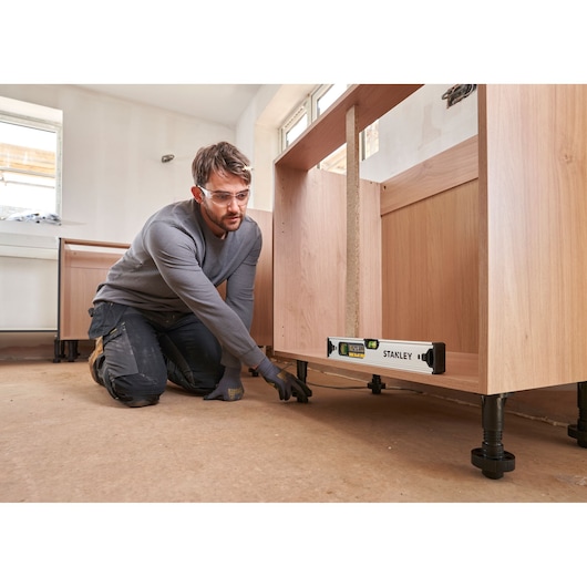 Stanley FMHT43671-1 spirit level used under wooden cabinet during installation, indoor scene.
