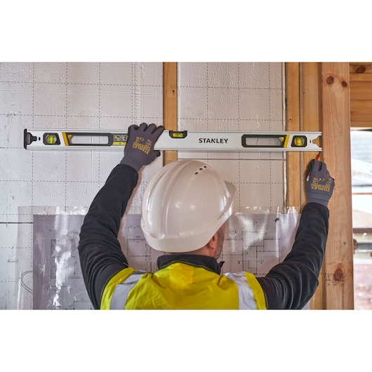 Photo of a worker using STANLEY FMHT43675-1 spirit level on wall, construction site background, product in use.