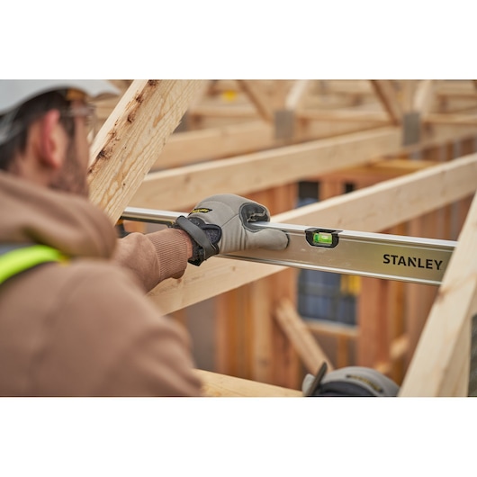 Stanley FMHT43679-1 level tool in use on wooden beams, worker wearing gloves and safety gear.