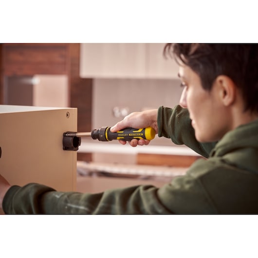 Stanley FMHT62692-0 screwdriver in use to assemble furniture, yellow and black handle, indoor setting.