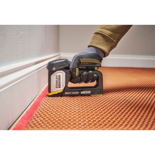 Photo of STANLEY FMHT70401-0 Multi-Tacker stapler in use, fastening carpet near skirting board.