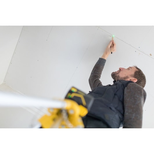 STANLEY FMHT77596-1 laser tool projecting green dot on ceiling during construction, person marking position.