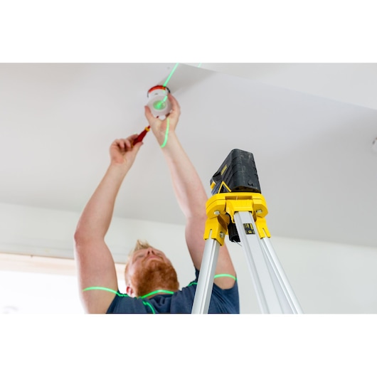 STANLEY FMHT77597-1 laser level tripod in use on ladder, showing green laser lines during ceiling installation.