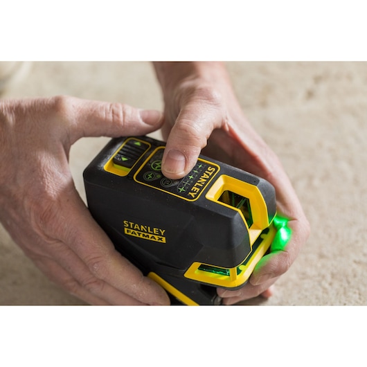 Photo of STANLEY FMHT77598-1 laser level, black and yellow, being held by hands, green light activated.
