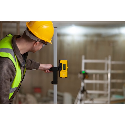 Photo of a worker using a STANLEY FMHT77653-0 laser detector attached to a rod at a construction site.