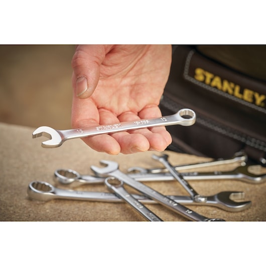 STANLEY FMMT13033-0 combination wrench held in hand, several wrenches on workbench, close-up photography.