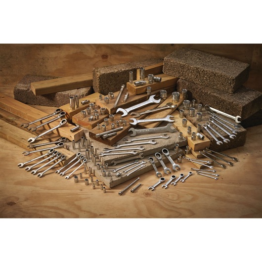 Various wrenches and sockets are arranged on wood and concrete blocks in a workshop setting.