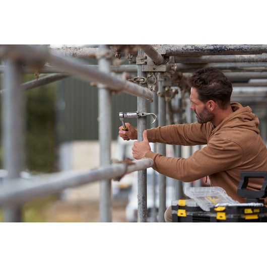 STANLEY FMMT82678-0 ratchet in use on scaffolding, worker in brown hoodie, STANLEY toolbox nearby.