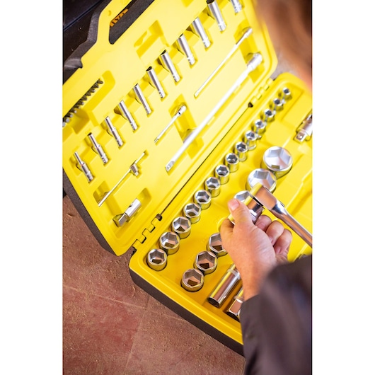 STANLEY FMMT82685-1 socket set with ratchet and sockets in yellow case, hand holding a tool, top view.