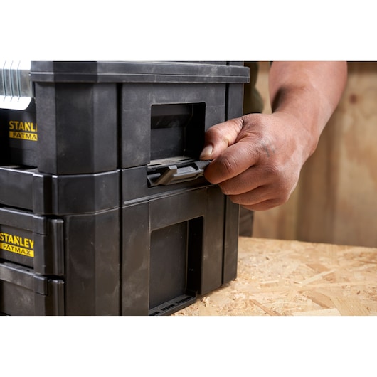 STANLEY FMST1-71969 toolbox latch being secured by hand, close-up angle on black plastic stacking toolboxes.