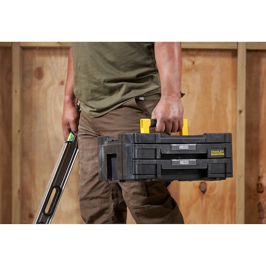 Photo of STANLEY FMST1-71969 tool box with yellow handle, carried by person, shown from the side indoors.