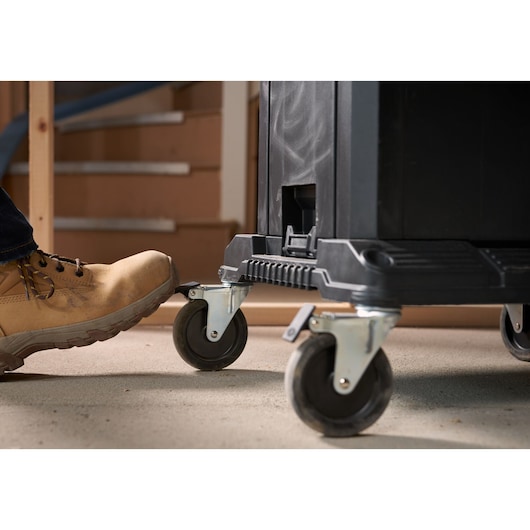 STANLEY FMST1-71972 tool chest caster wheels close-up with foot pressing brake in workshop.