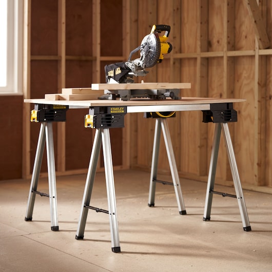 STANLEY FMST1-75763 folding metal saw horses used to support a worktable with a saw, shown in a workshop.