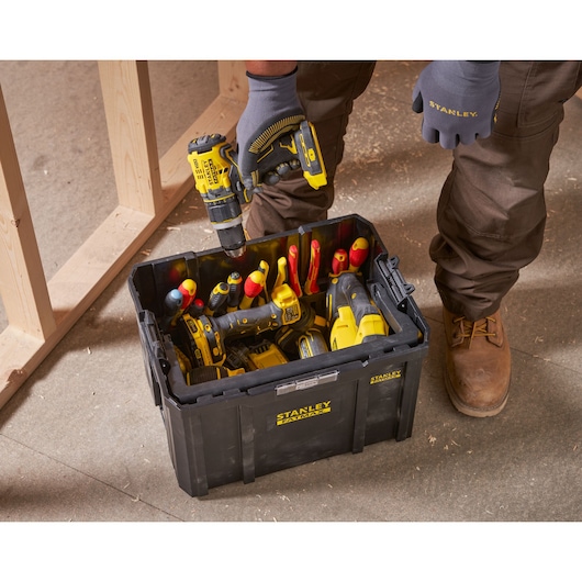 STANLEY FMST1-75794 black toolbox on jobsite floor, filled with hand tools and power tools, person holding drill.