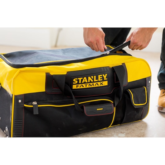 STANLEY FMST82706-1 large yellow and black soft tool bag with zipper, being opened by hand.